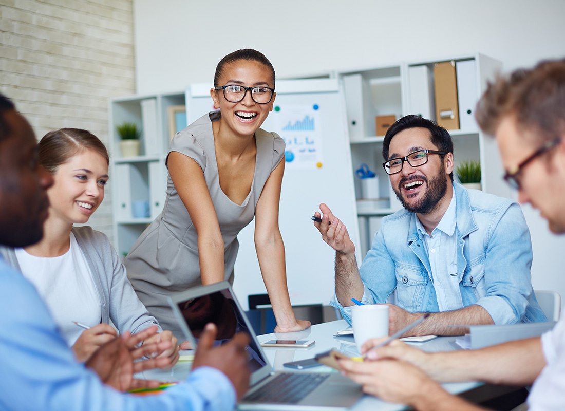 Employee Benefits - Small Group of Happy Employees Sitting Around a Table in the Office During a Business Meeting Having a Discussion