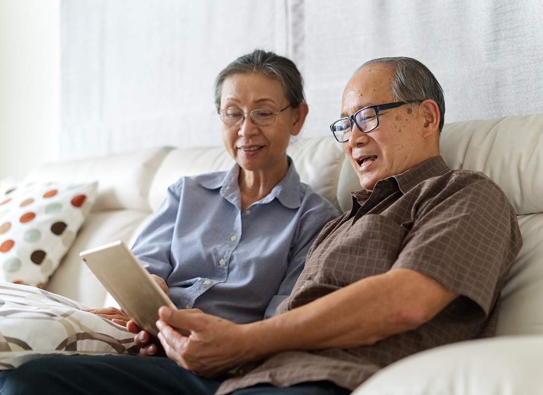 Service Center - Portrait of an Elderly Couple Wearing Glasses Sitting on the Sofa at Home While Using a Tablet